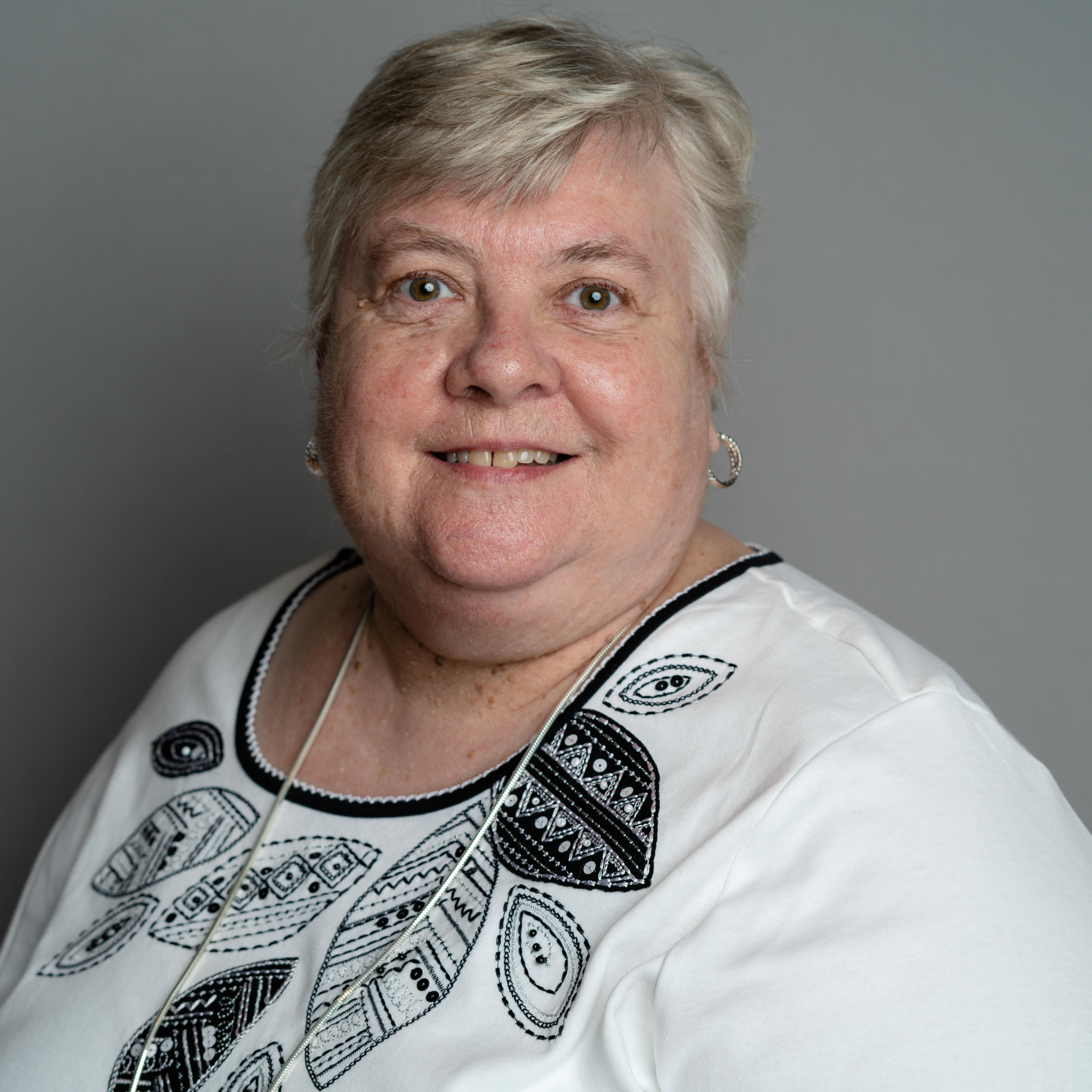 Professional portrait of a woman smiling, wearing a black and white shirt against a gray background.